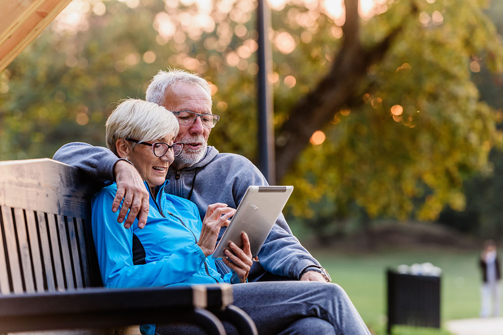 Older couple relaxing outdoors with a tablet