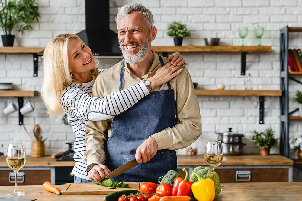 Smiling couple cooking together and enjoying food again after full arch dental implants